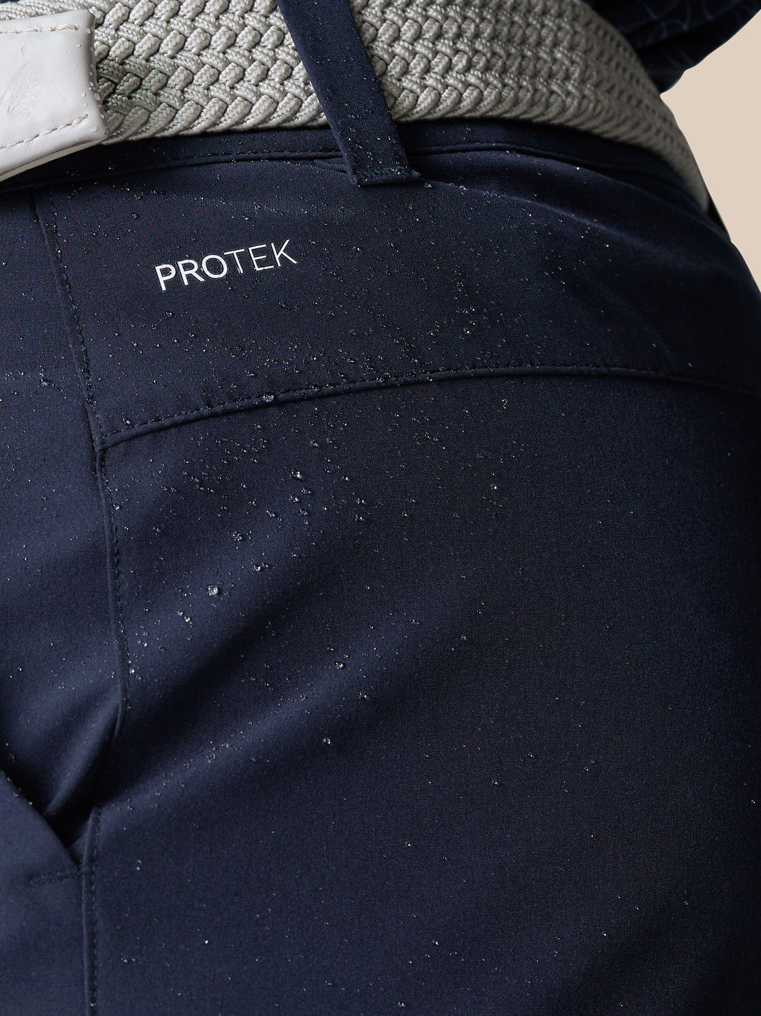 Close up of navy golf shorts fabric with visible ProTek branding and water droplets