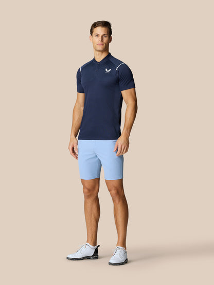 Male model wearing sky blue Golf Club Shorts with a navy top against a beige background