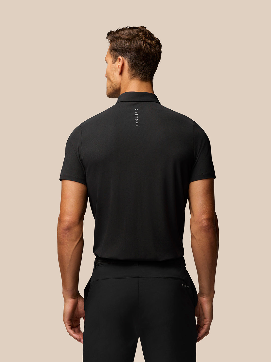 Back view of a man wearing a black Golf Club Essential Polo with Castore branding down the upper back.