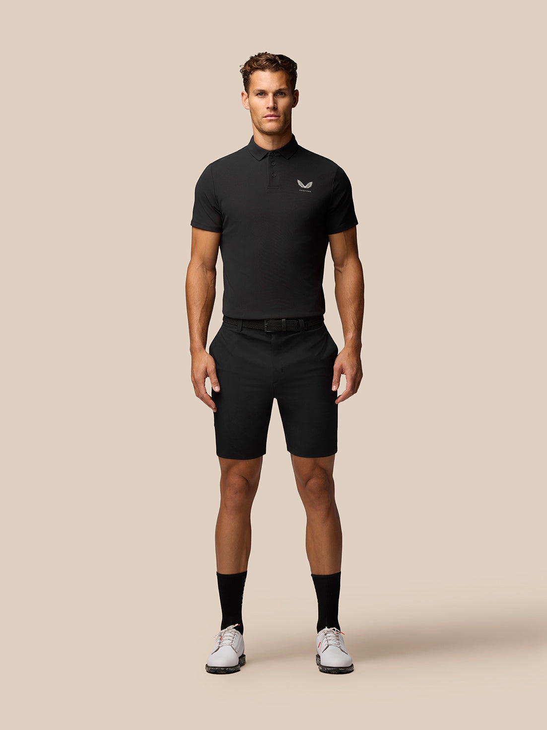 Front view of a man in a black Golf Club Essential Polo with a small Castore logo on the left chest and black shorts.