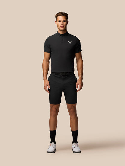 Front view of a man in a black Golf Club Essential Polo with a small Castore logo on the left chest and black shorts.
