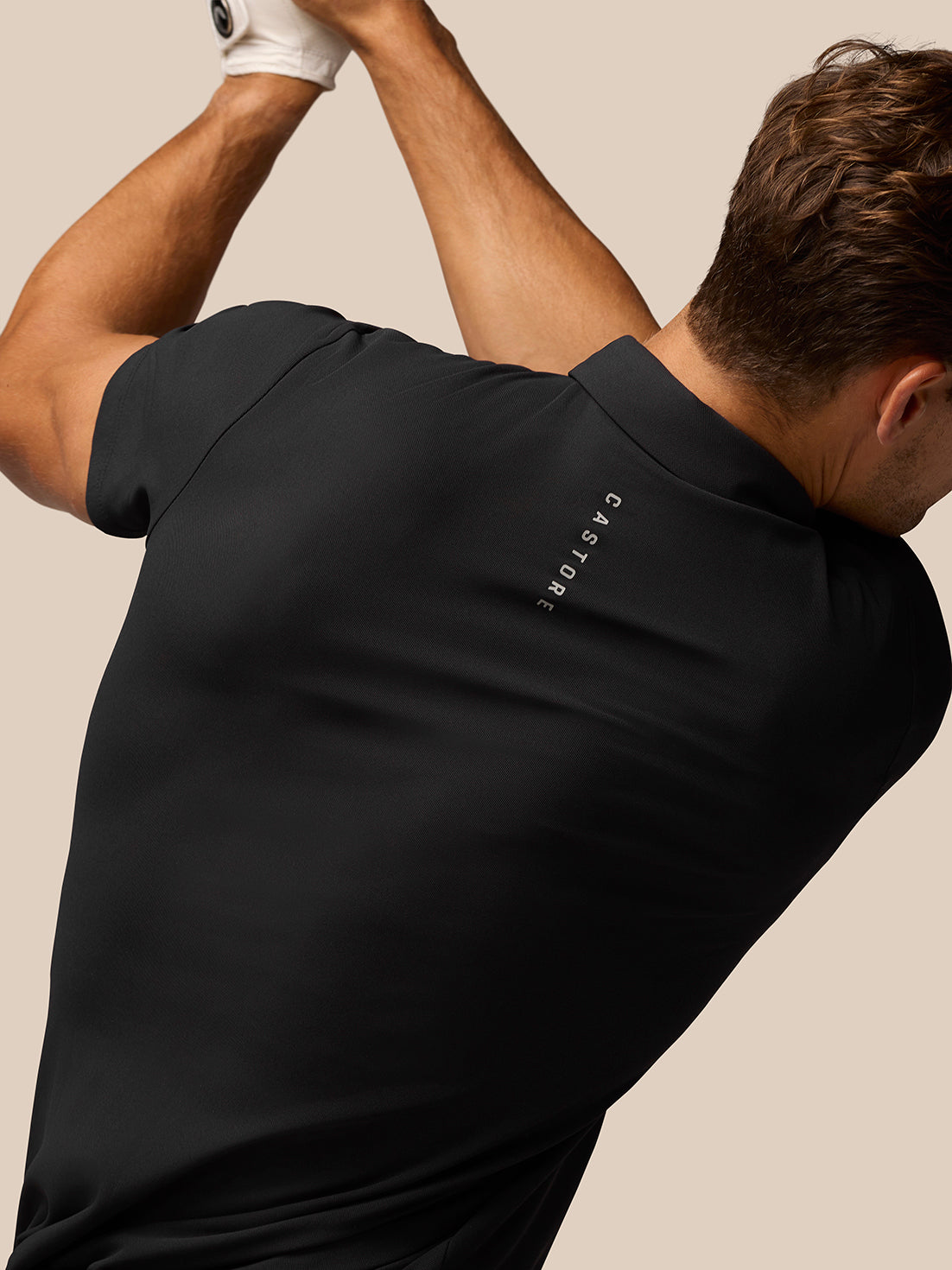 Back view of a man in a black Golf Club Essential Polo with vertical Castore branding along the upper back.