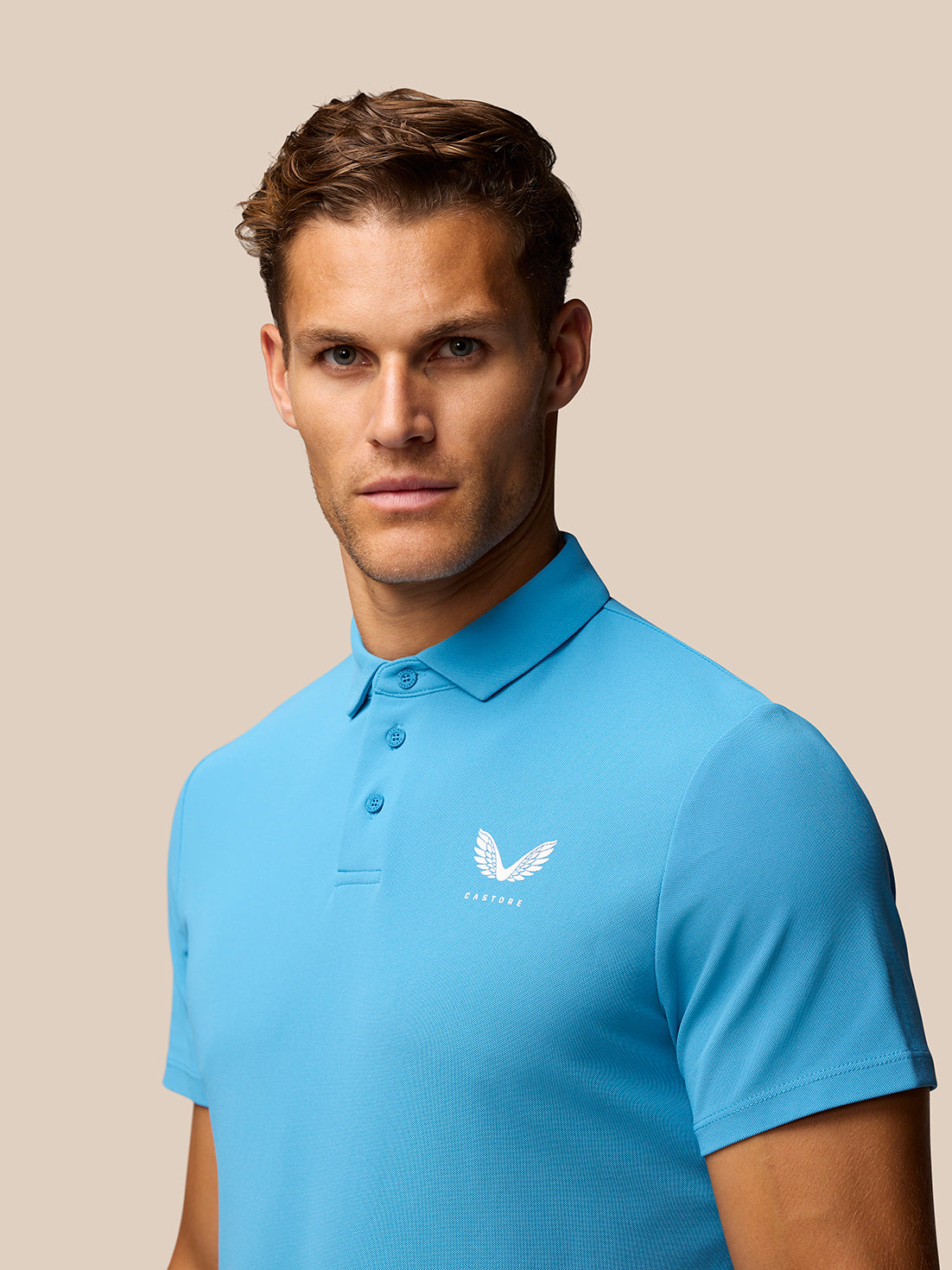 Close-up of man in corn blue Club Golf Polo highlighting collar and Castore logo.