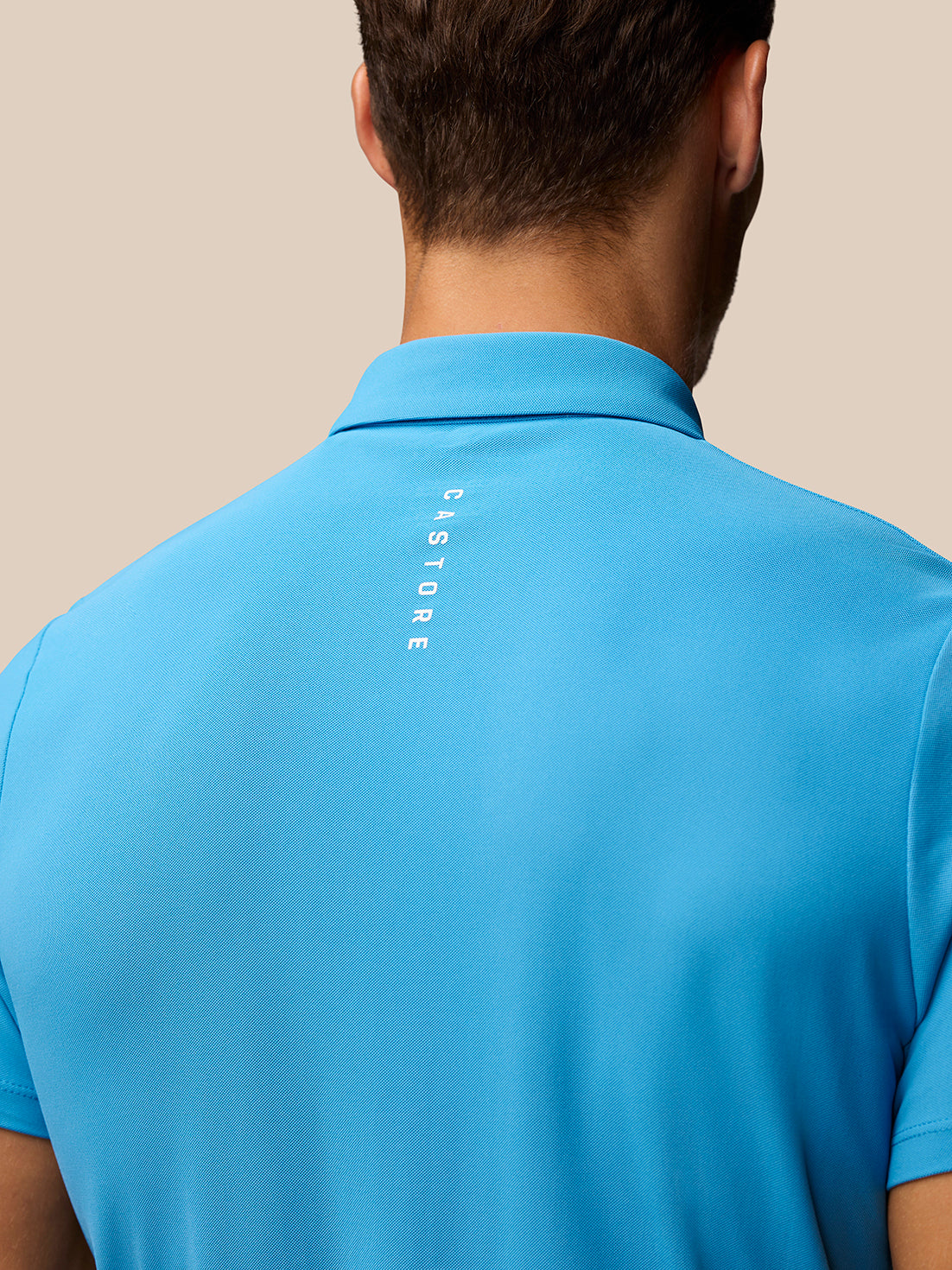 Back view of man in corn blue Club Golf Polo with CASTORE branding running down the back.