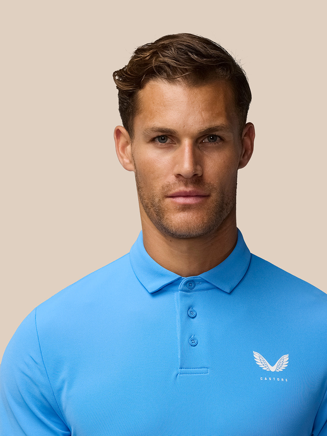 Close-up portrait of a man wearing the Cool Blue Golf Club Essential Polo with Castore logo on the chest.