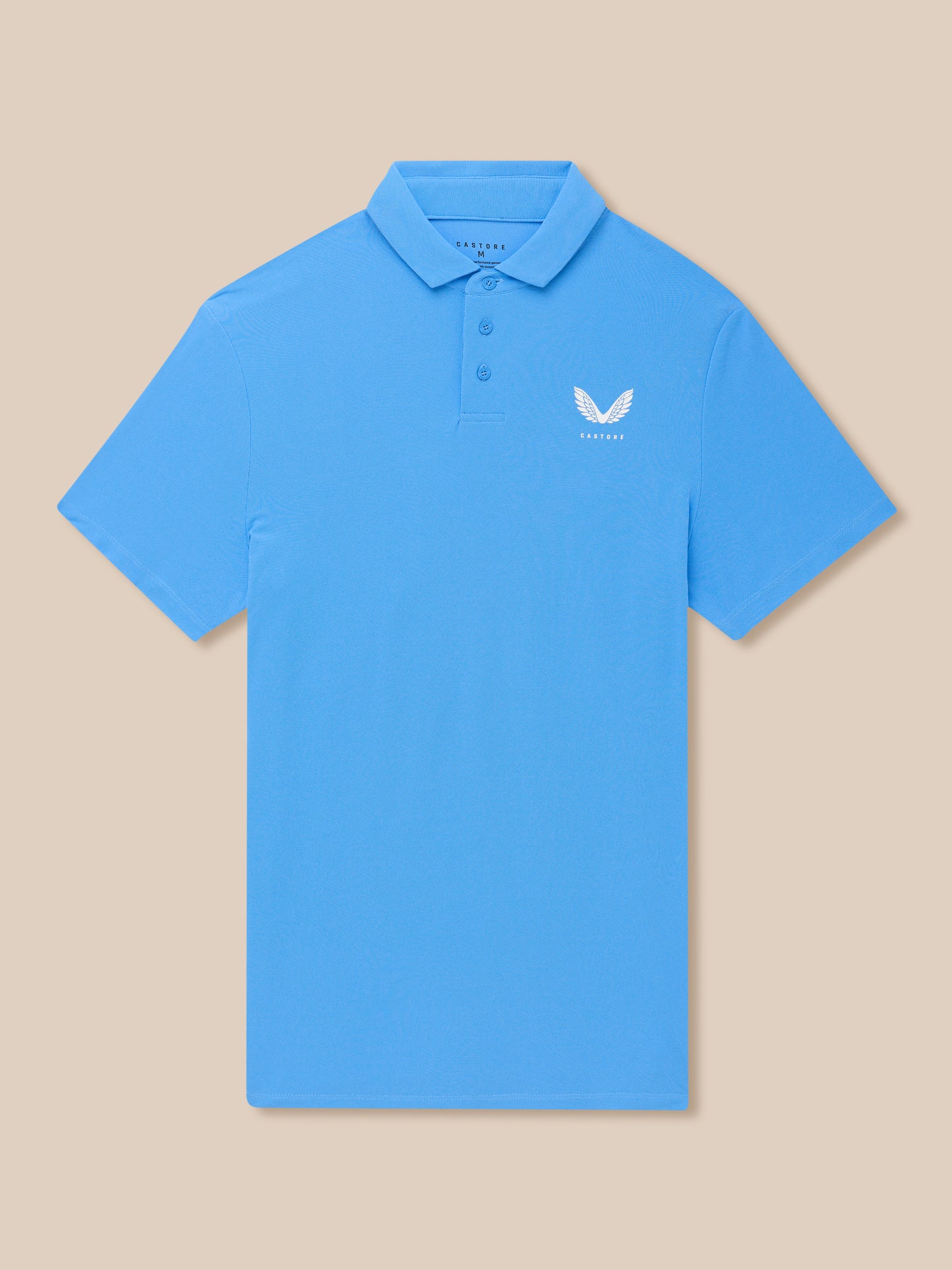 Close up of a light blue golf polo with a collar and three button placket, left chest Castore logo on a beige background