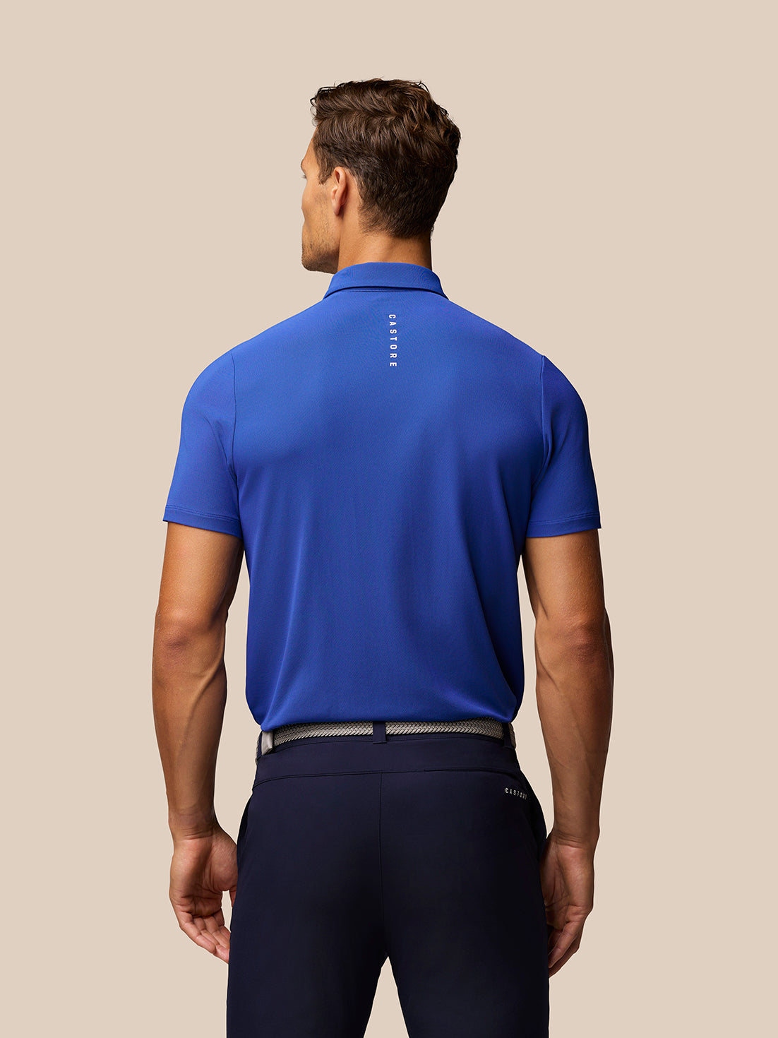 Back view of royal blue golf polo on a male model with Castore branding running down the back