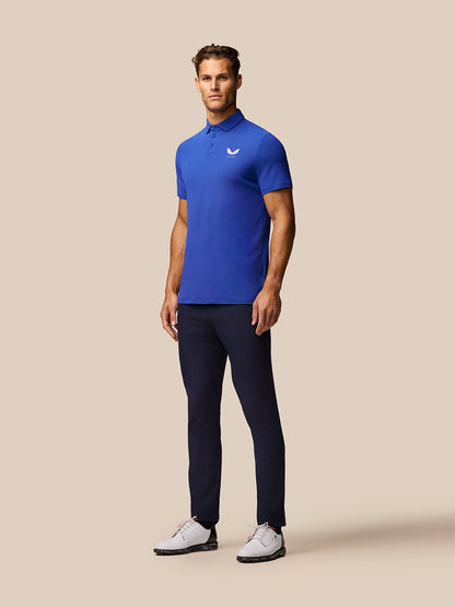 Full body of a man wearing royal blue Club Golf Polo with navy pants and white shoes, Castore logo on chest.