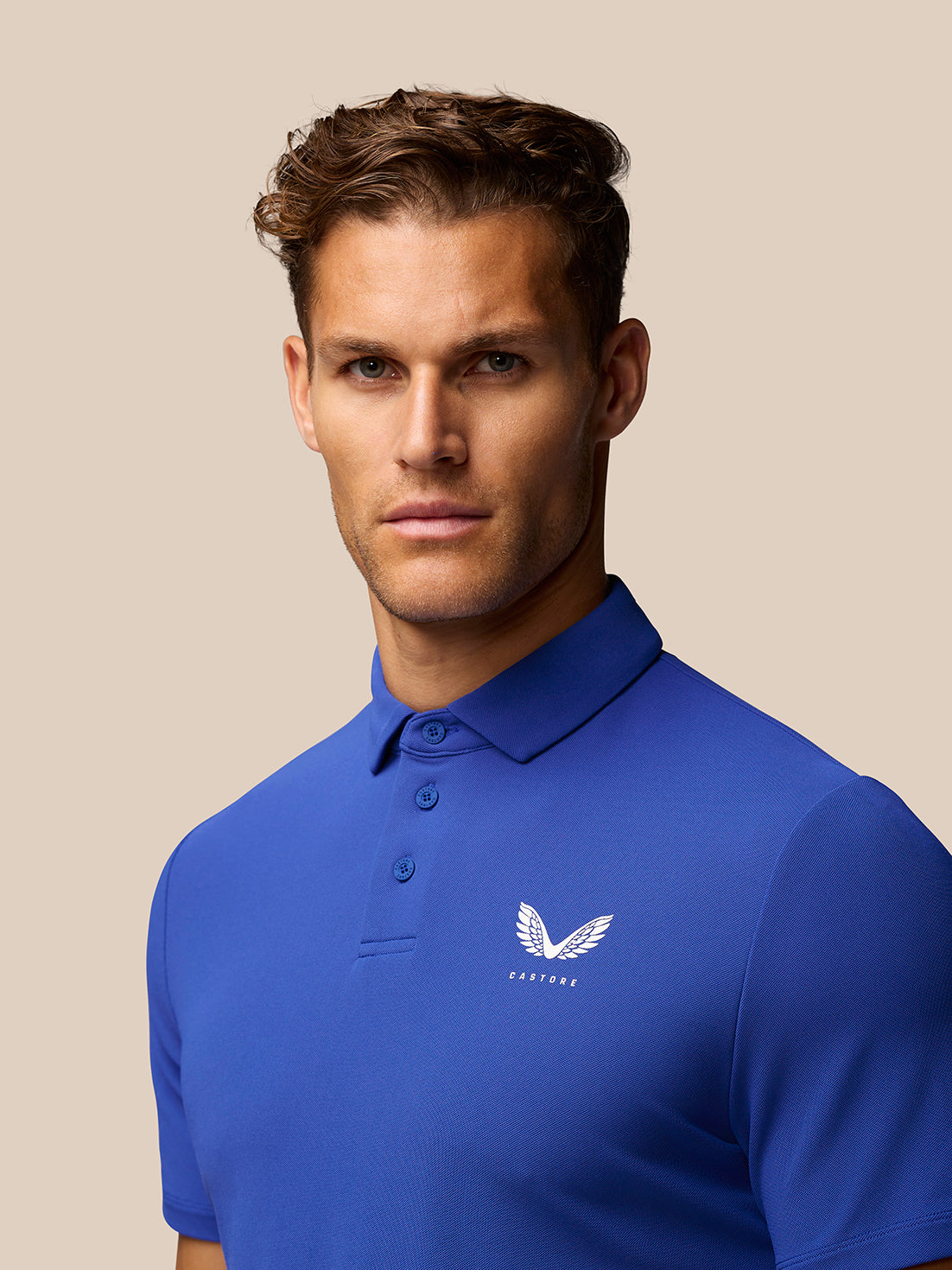 Male model wears royal blue Club Golf Polo with pointed collar and three button placket; Castore logo on left chest.