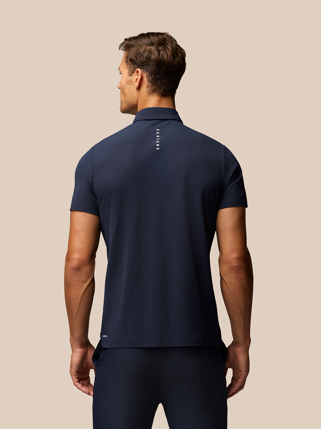 Male model wearing midnight navy golf polo and matching shorts; back view shows Castore branding along the upper back and Aertek branding at the lower back