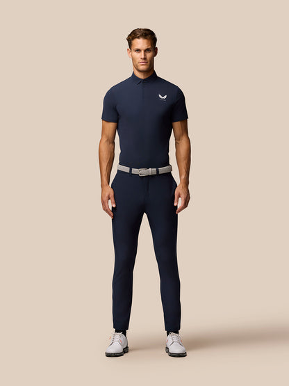 Front view of a man wearing navy golf polo with Castore logo on the left chest, tucked into dark trousers with a light belt