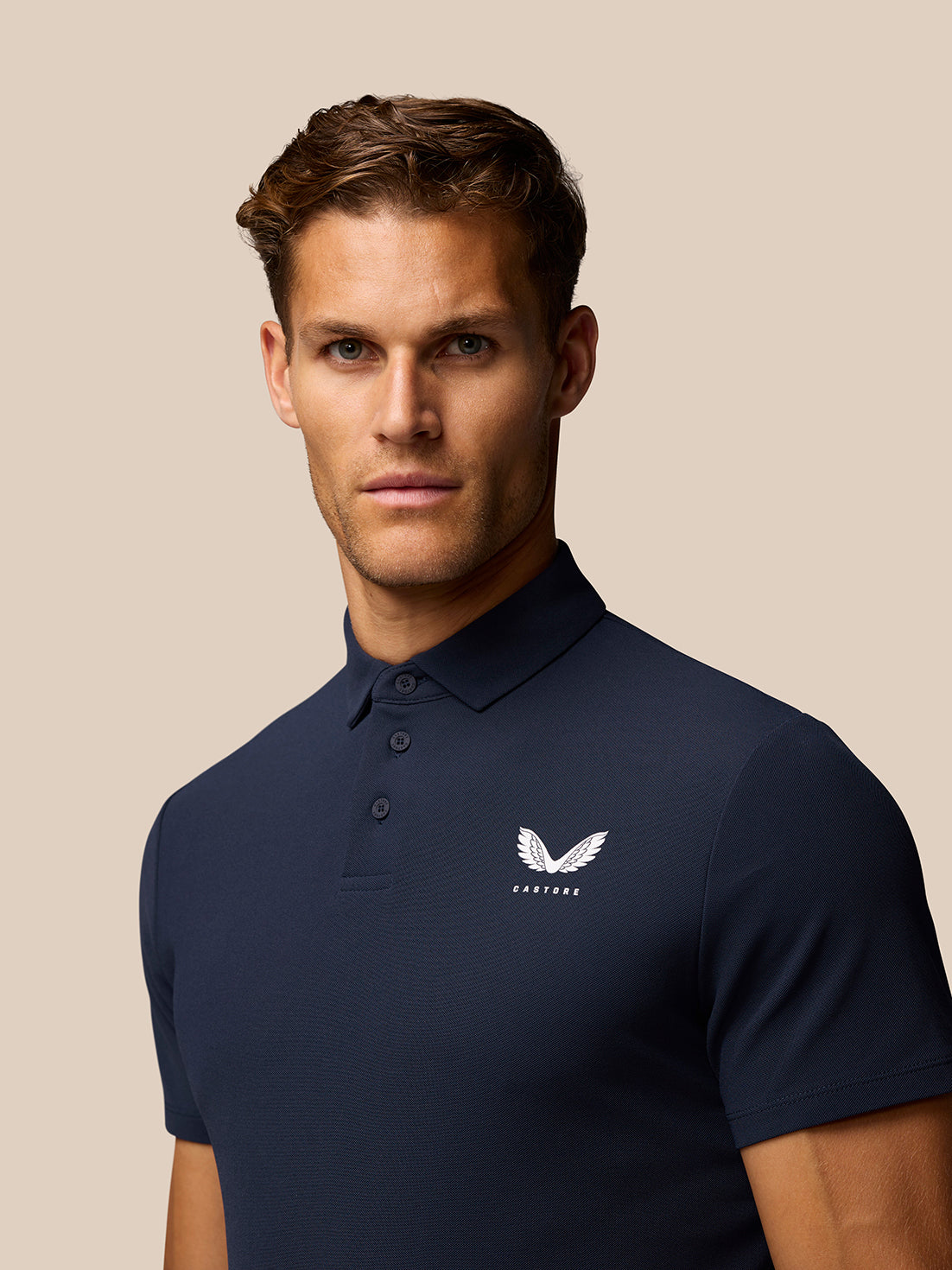 Male model wearing a navy golf polo with three-button placket and Castore logo on the left chest