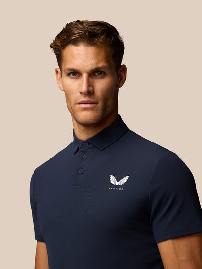 Male model wearing a navy golf polo with three-button placket and Castore logo on the left chest