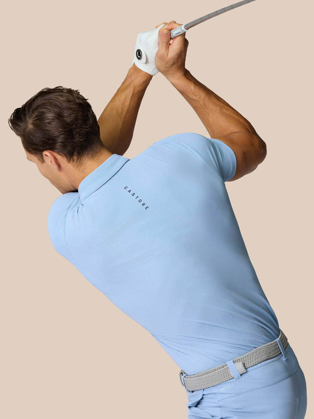 Golfer in sky blue polo mid swing with branding on back