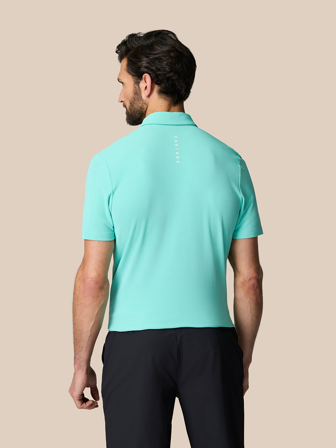 Back view of a man in a light aqua Golf Club Essential Polo showing branding along the upper back