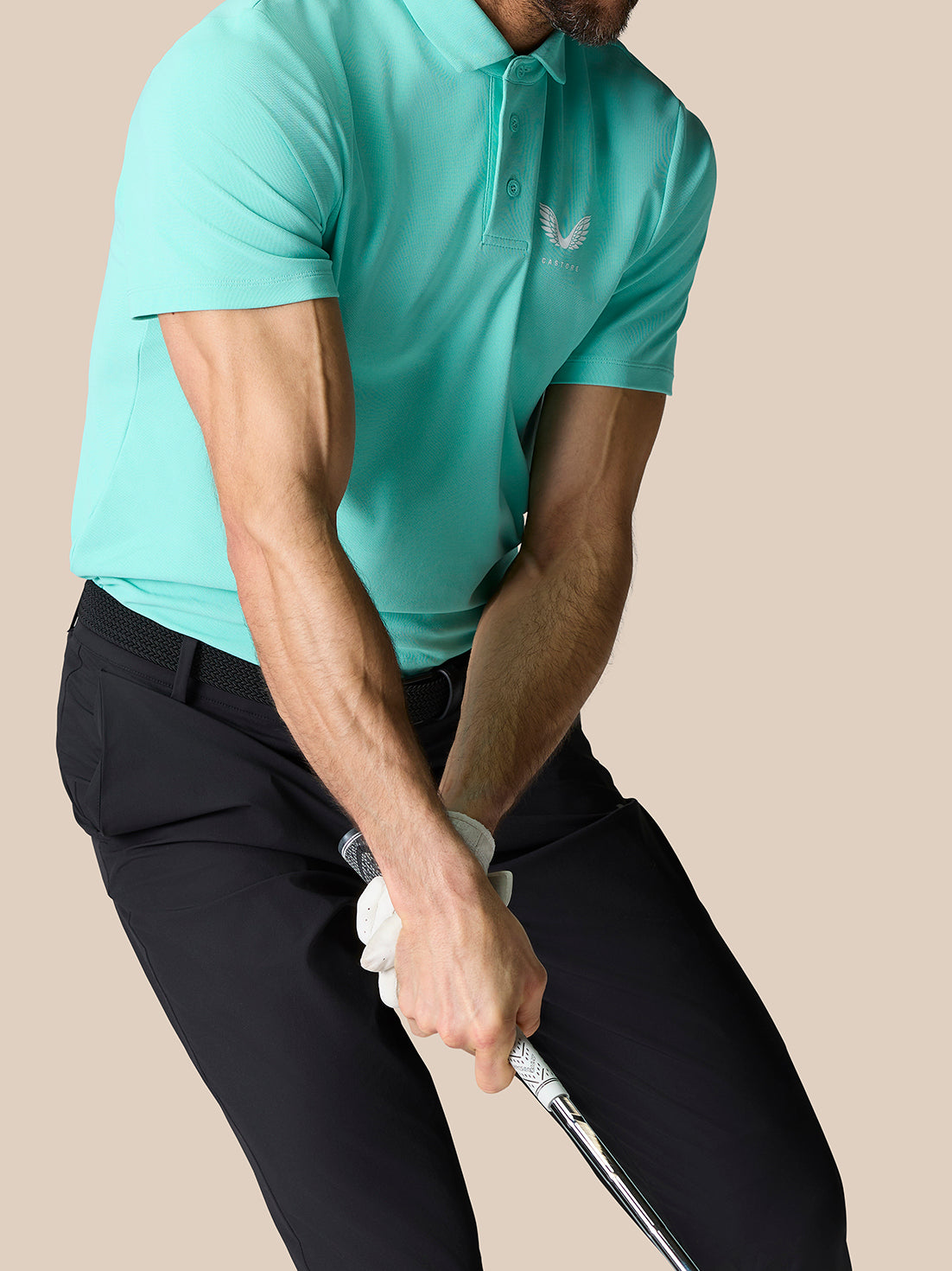 Male golfer wearing light aqua Golf Club Essential Polo with Castore branding gripping a golf club.