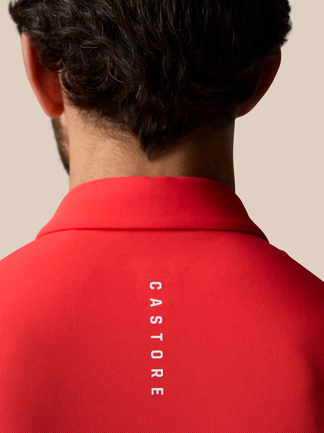 Back of the red Golf Club Essential Polo highlighting vertical Castore branding along the spine.