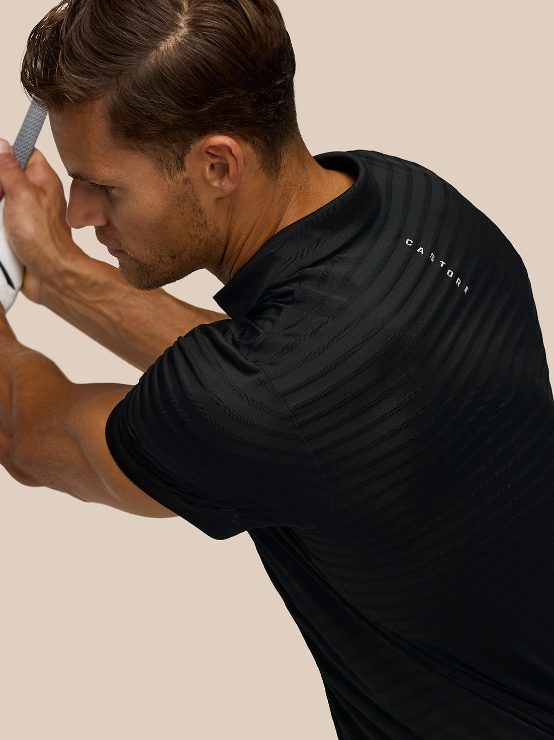 Back view of a man wearing a black Pinnacle Pique Stripe Polo with a striped knit pattern and Castore branding on the upper back.