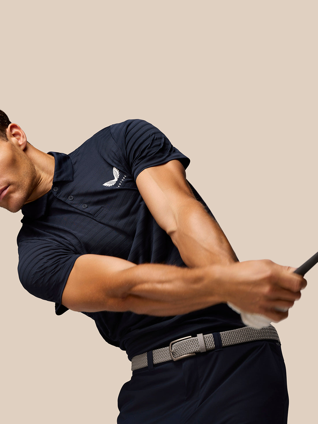Side view of a man in navy Pinnacle Pique Stripe Polo mid swing with a golf club and Castore logo on the left chest.
