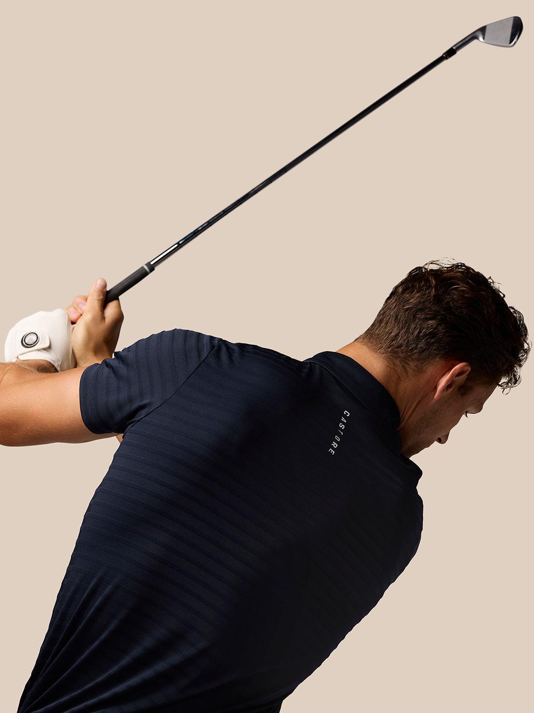 Back view of a man in a navy Pinnacle Pique Stripe Polo with vertical Castore branding along the spine.
