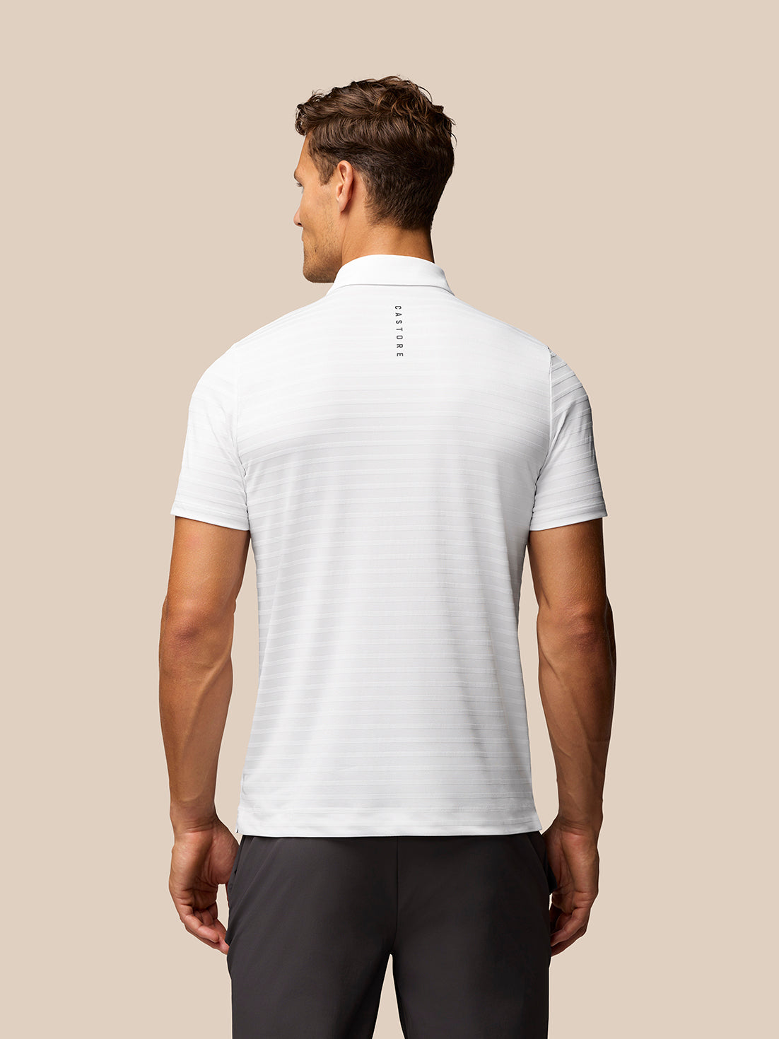 Back view of a male model wearing a white textured pique stripe polo with subtle stripe pattern