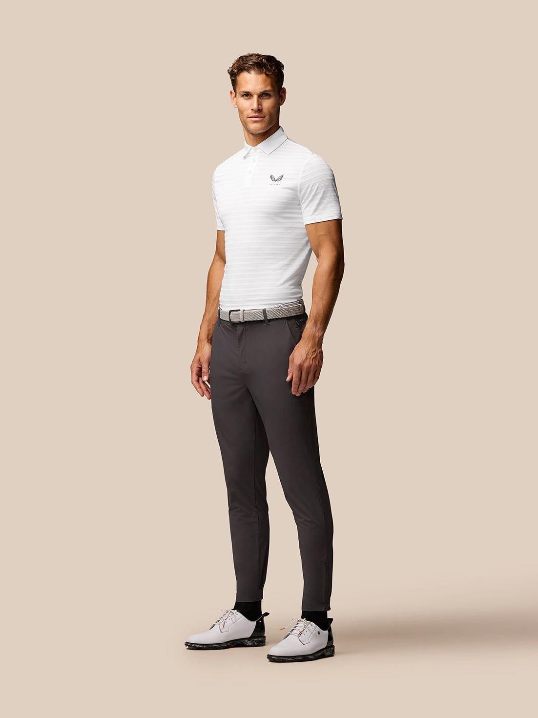 Male model wearing white Golf Pinnacle Pique Stripe Polo with subtle stripes and Castore logo on chest
