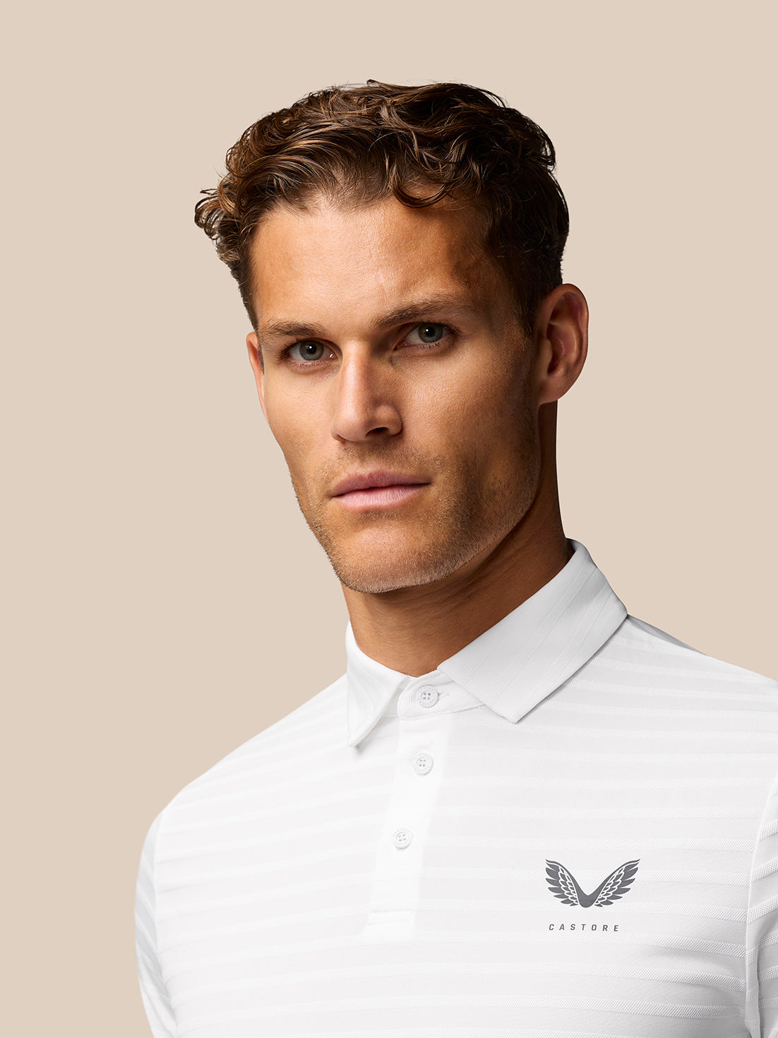 Male model wearing white textured pique stripe golf polo with Castore logo on left chest.