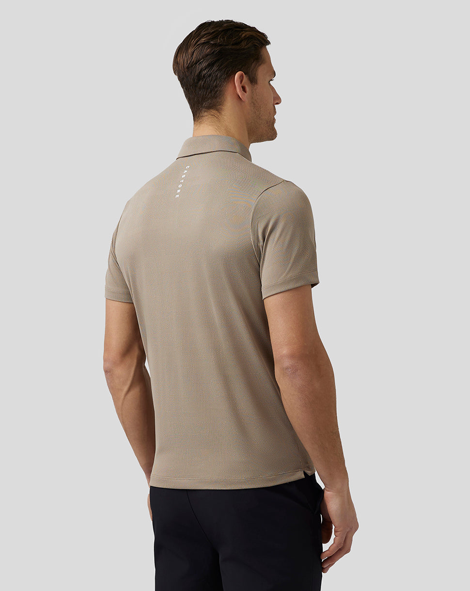 Back view of beige Pinnacle Knit Polo on a man showing Castore branding on the upper back and Aertek branding at the lower back