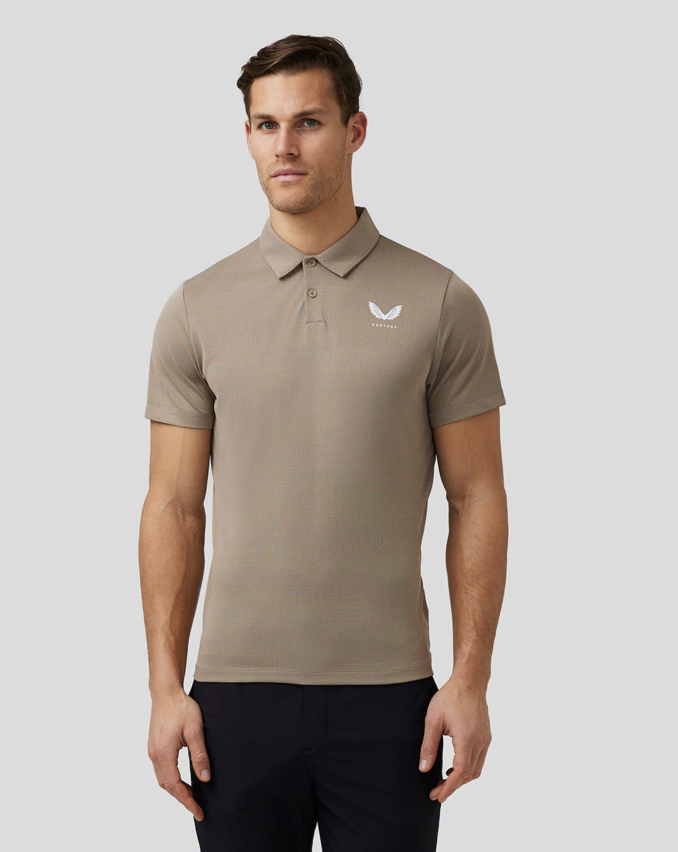 Full body front view of a man wearing beige Pinnacle Knit Polo with left chest logo and dark trousers