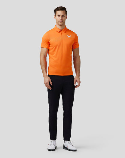 Waist up front view of a man wearing a bright orange golf polo with a three button placket and left chest logo