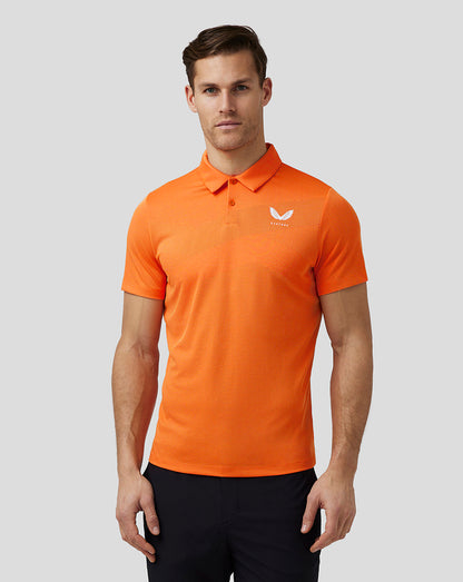 Full body front view of a man in a bright orange golf polo with black pants and white shoes