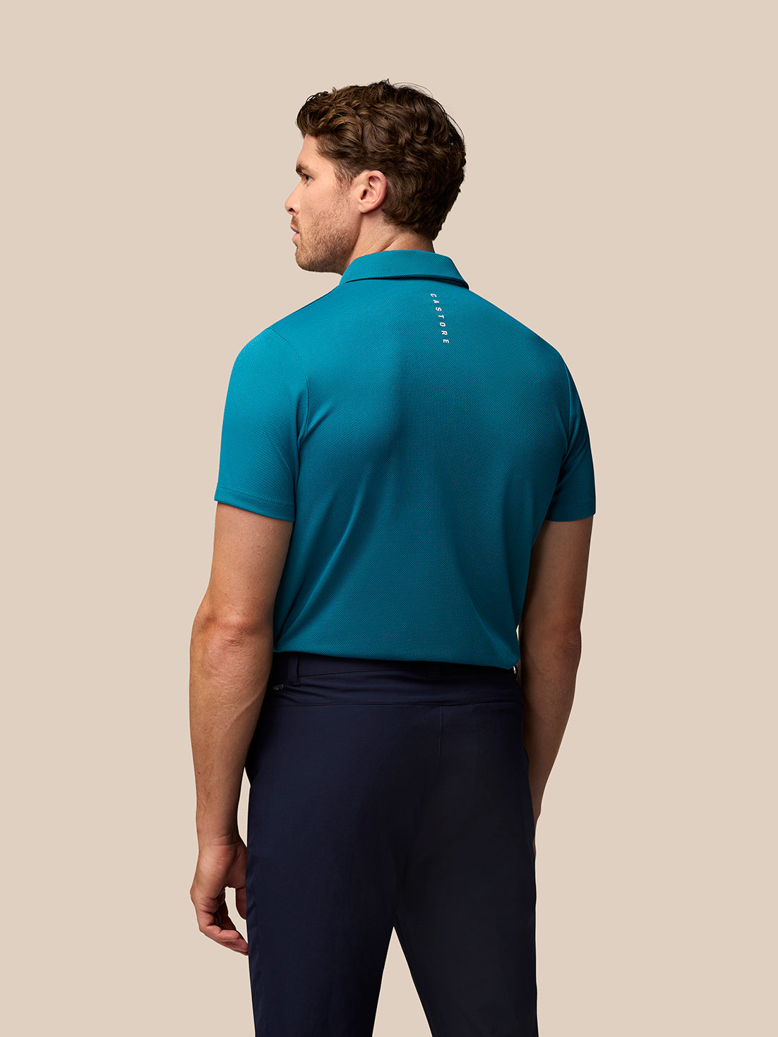 Back view of teal Pinnacle golf polo showing diagonal knit texture and Castore branding along the upper back.
