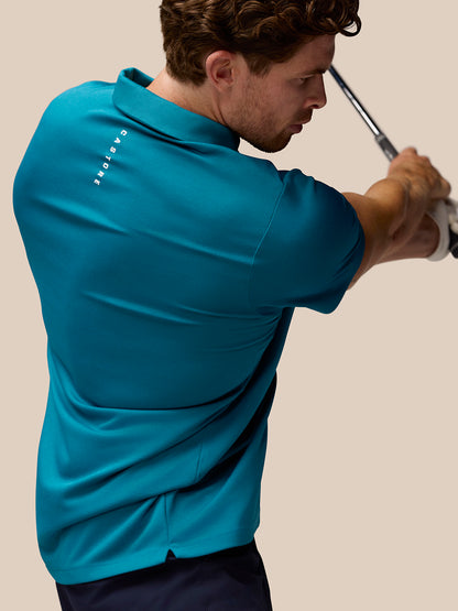 Back view of a man in dark aqua Pinnacle golf polo mid swing with a golf club.