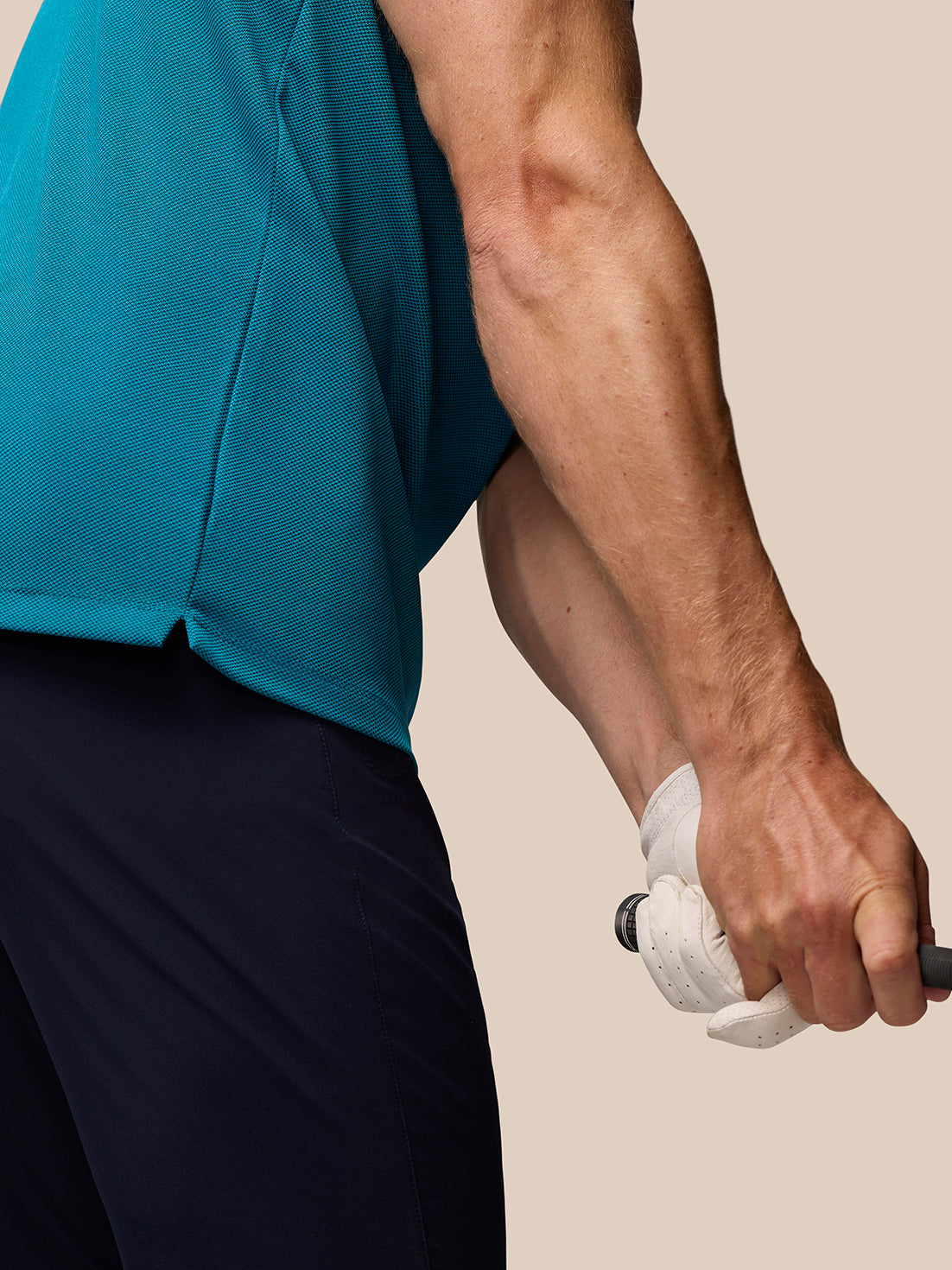 Close-up of a man in dark aqua Pinnacle golf polo showing textured knit fabric as he grips a club.