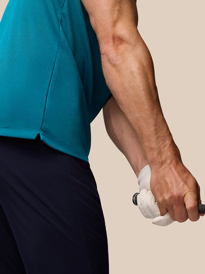 Close-up of a man in dark aqua Pinnacle golf polo showing textured knit fabric as he grips a club.