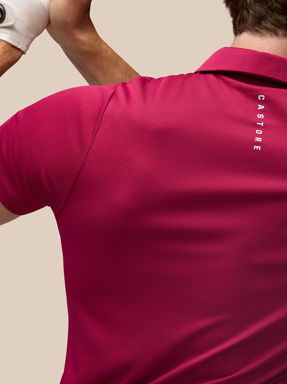 Back view of a man wearing a pink Pinnacle Golf Polo with Castore branding along the upper back.