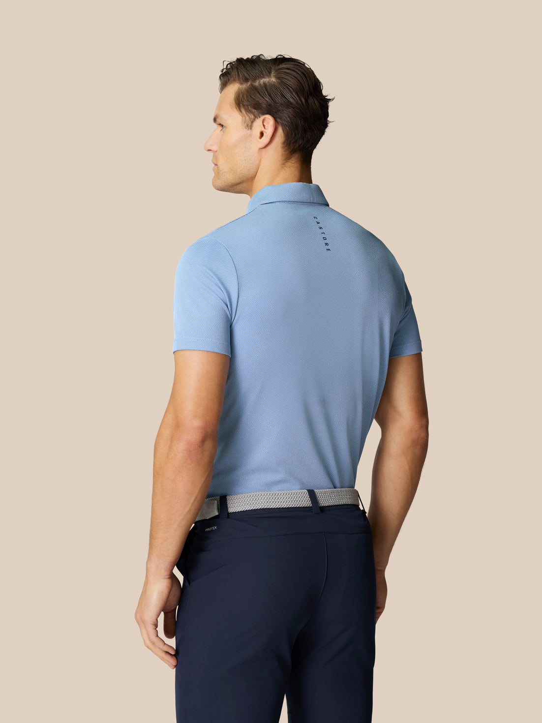 Man in sky blue golf polo shown from the back with breathable knit fabric and branding at the upper back.