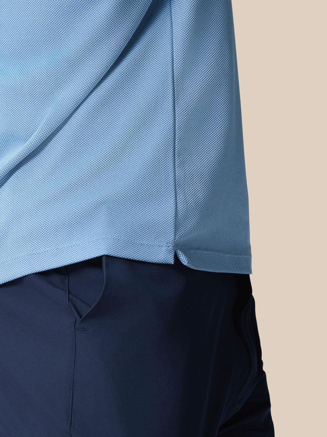Close-up of light blue polo knit showing texture and curved hem with side slit, navy shorts visible.