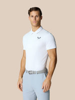 Male model wearing white Golf Pinnacle Polo with Castore logo on chest and light blue pants against a beige backdrop