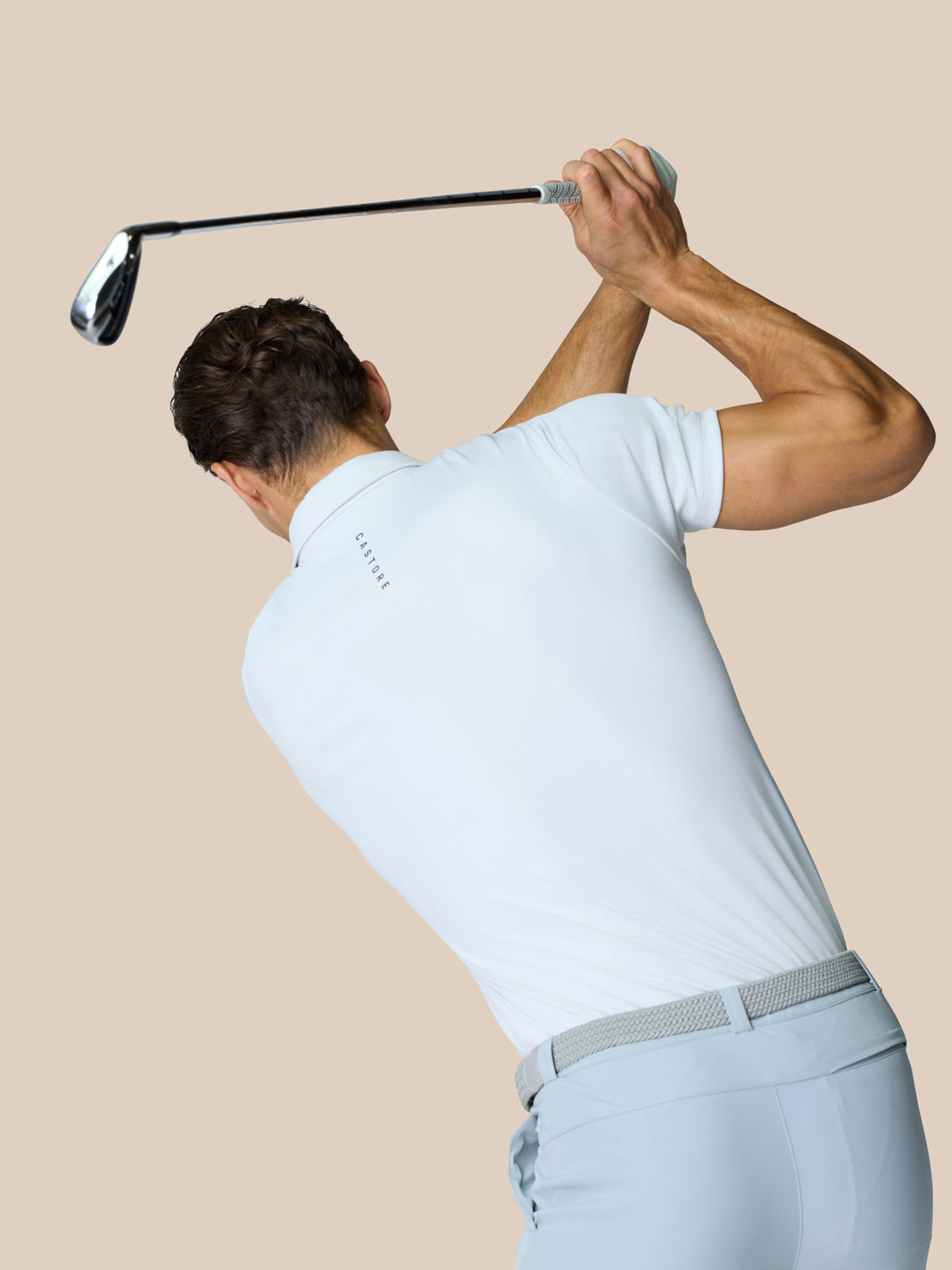 Back view of a golfer in the white Golf Pinnacle Polo with branding at upper back mid swing