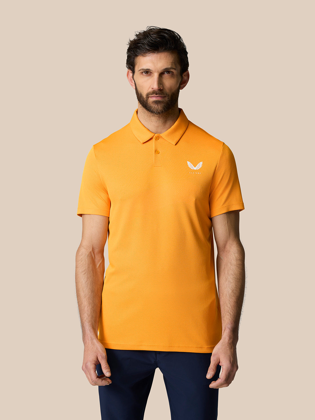 Close-up of orange Golf Pinnacle Polo Mango on a male model showing the chest logo.