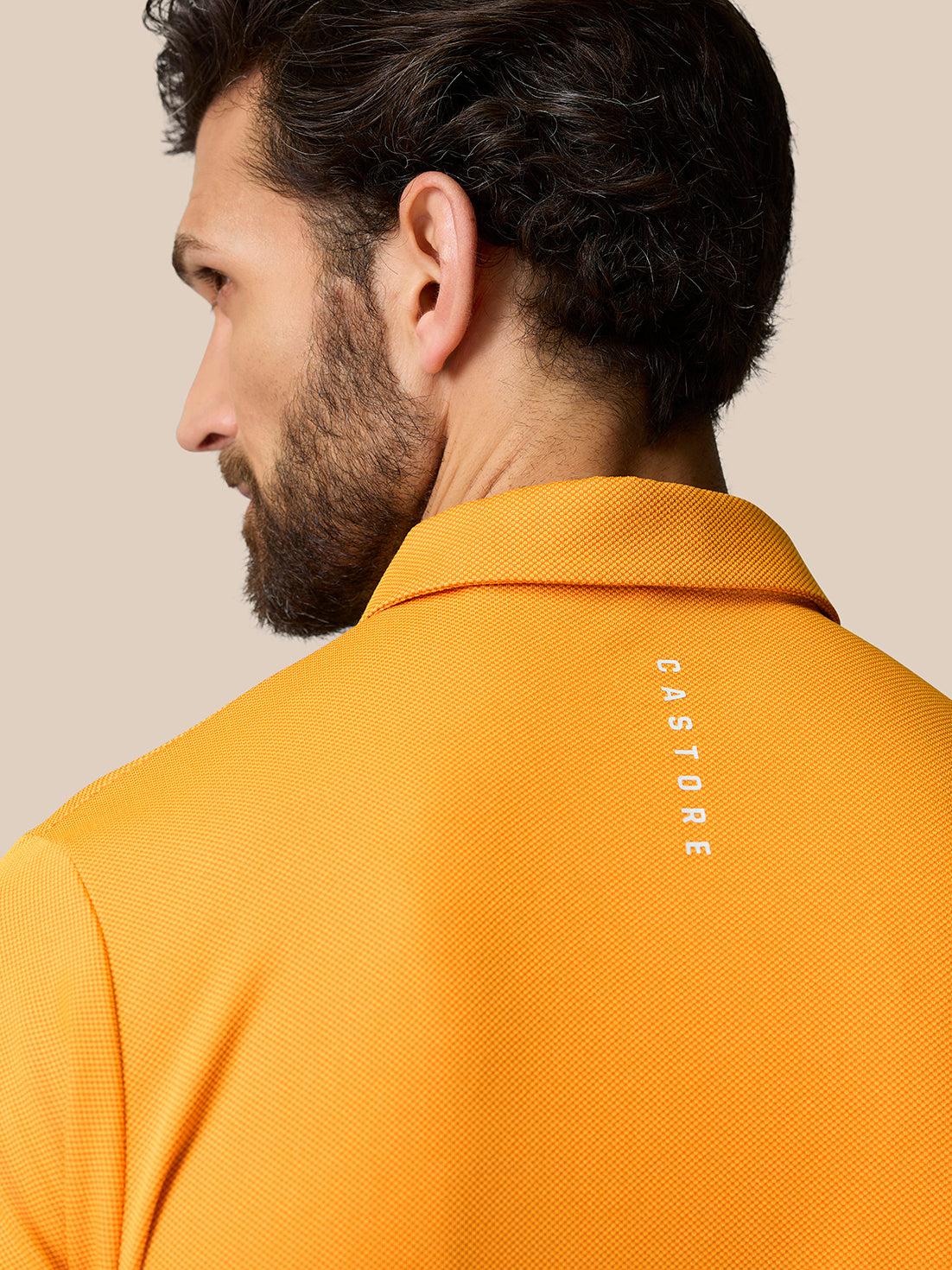 Back view of the orange Golf Pinnacle Polo Mango showing Castore branding along the upper back.