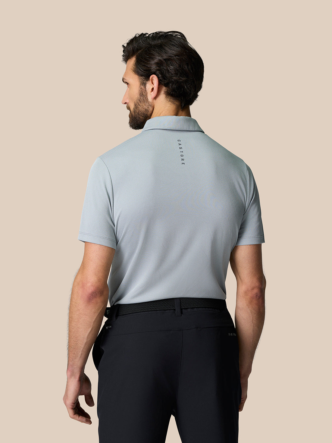 Back view of a man in a mid grey engineered knit polo with branding on the upper back.