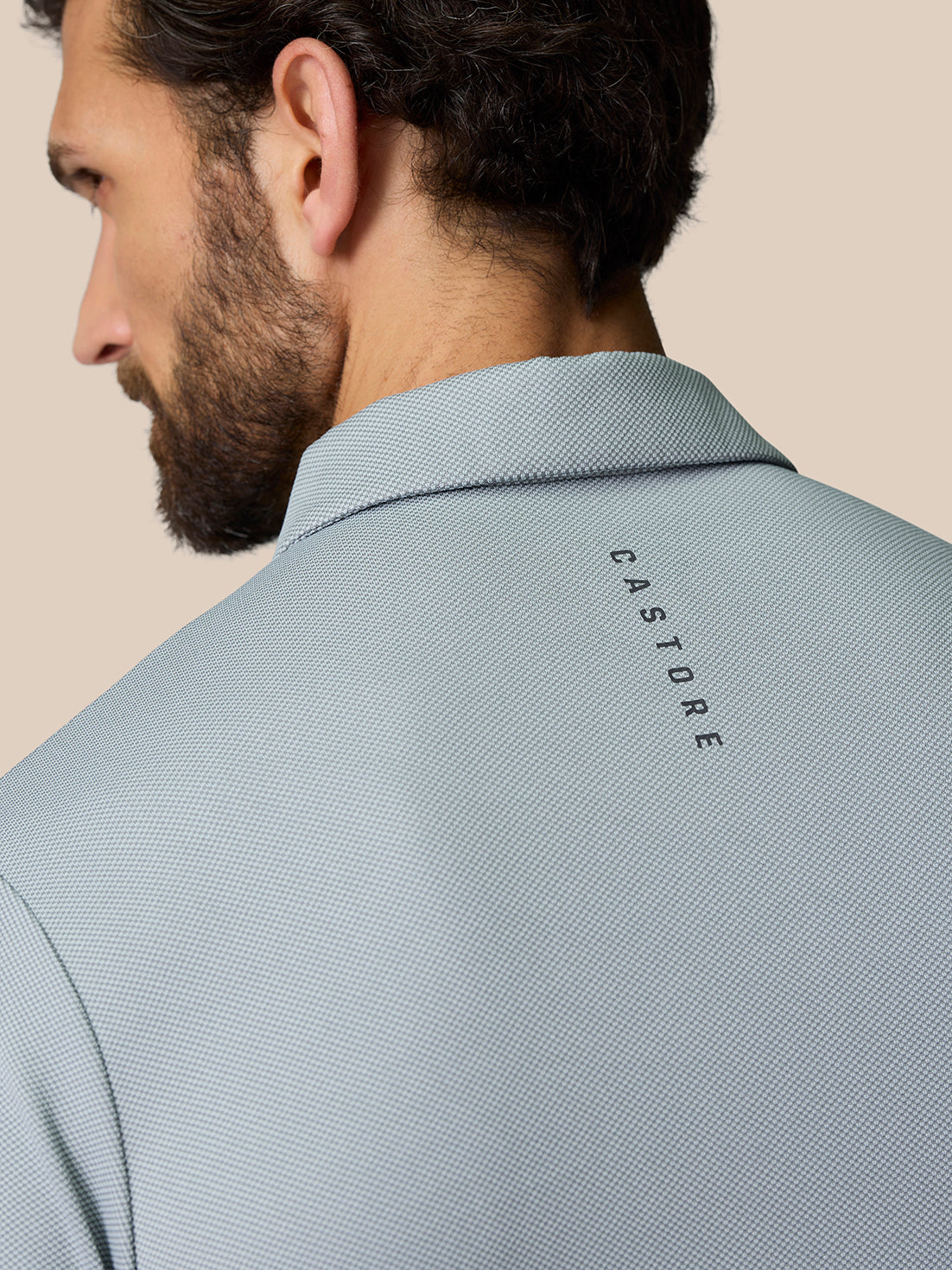 Back view of a man in a light grey polo showing CASTORE branding along the upper back