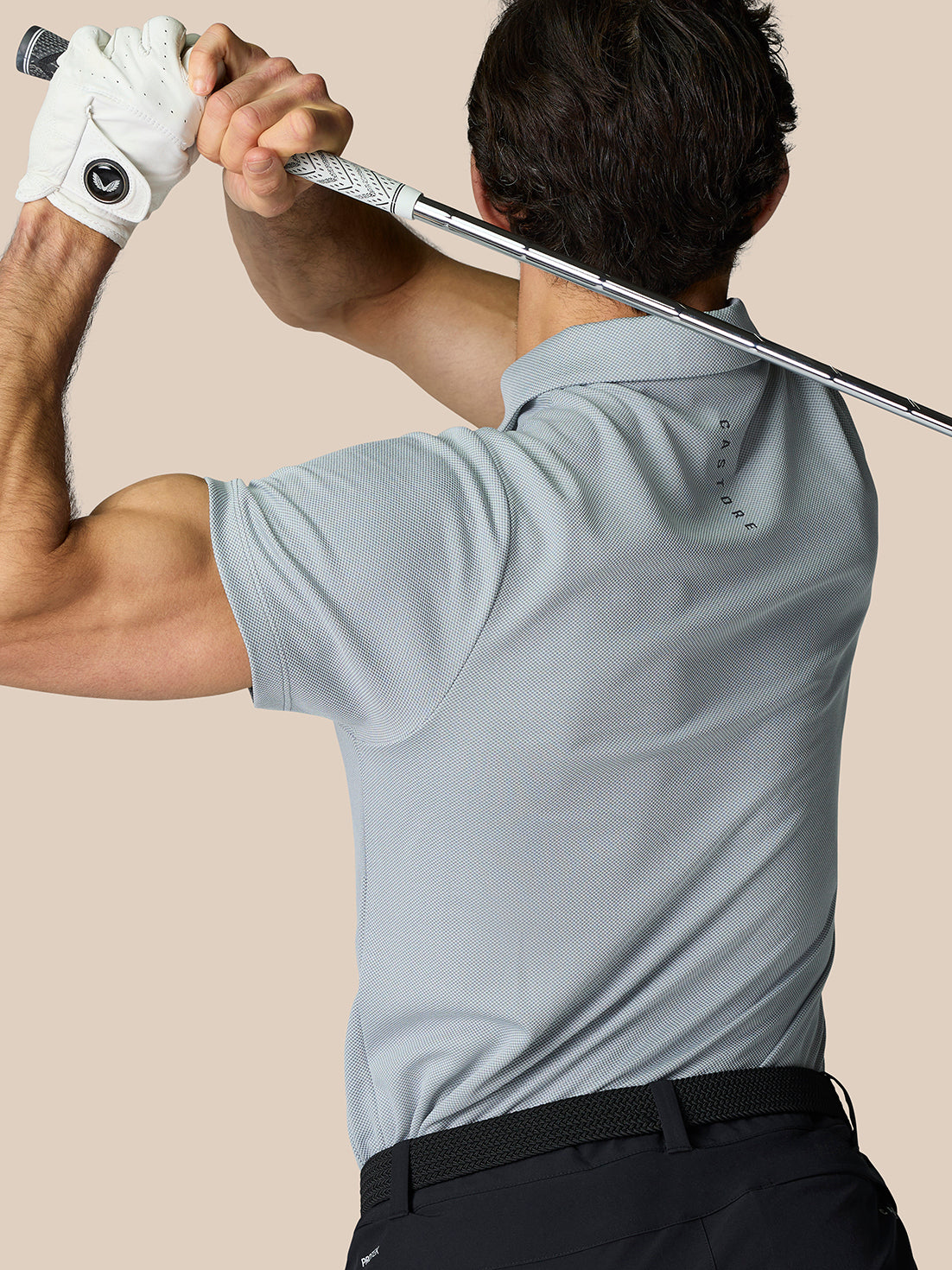 Golfer in mid grey polo shown from behind starting a swing with a white glove on the left hand.