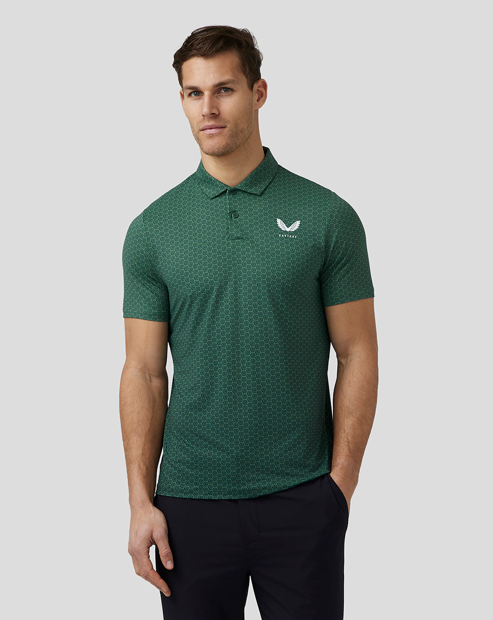 Full front view of a man in a green hex pattern golf polo with a white left chest logo, black pants, and white golf shoes.