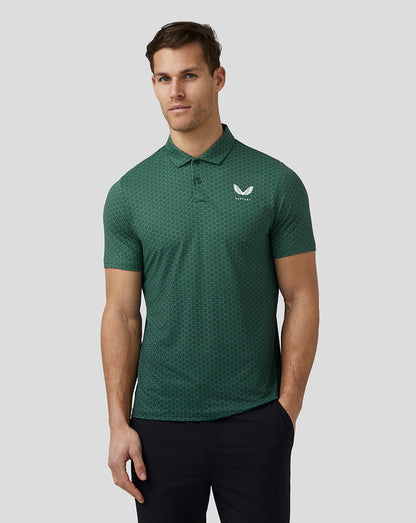 Full front view of a man in a green hex pattern golf polo with a white left chest logo, black pants, and white golf shoes.