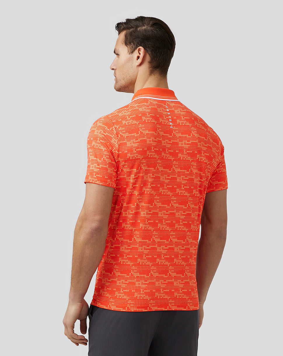 Back view of a male model wearing a bright orange printed golf polo with a pixelated pattern and a drop back hem.