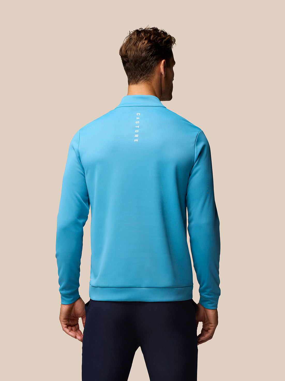 Back view of corn blue golf top showing vertical Castore branding down the center back