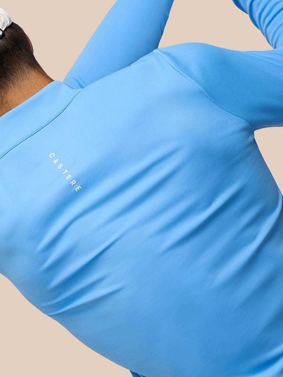 Side view of a model in a light blue Club Classic quarter zip top with Castore logo on the left chest and a white cap.